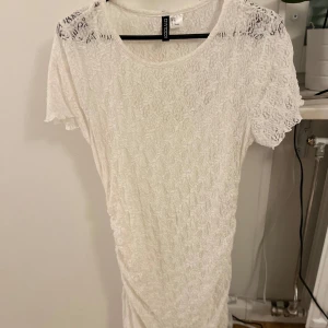 Vit spetsklänning från H&M - Säljer en söt vit spetsklänning från H&M. Klänningen har korta ärmar och ett vackert spetsmönster över hela plagget. Perfekt för en somrig look eller en elegant touch till vardagsoutfiten.