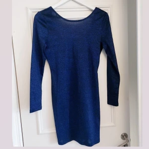 Blå glittrig klänning från H&M  - Snygg blå glittrig klänning med långärmad design. Perfekt för en kväll ute med vänner. Den har en figurnära passform som framhäver silhuetten.