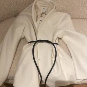 Vit kappa  - Elegant vit kappa  Jackan har en knytning i midjan och långa ärmar, storlek XS/S prislappen kvar