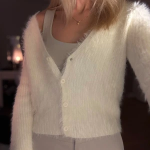 Vit fluffig kofta från Zara - Säljer en supermjuk och fluffig vit kofta från Zara🤍. Den har en v-ringad design med knappar framtill och långa ärmar. Den är liten i storleken, därav i storlek L, men är som en S. Prislapp är borttagen men aldrig använd, bara provad! 