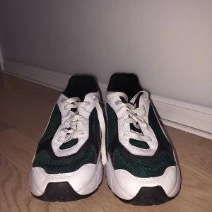 Grönvita sneakers från Puma - Snygga sneakers från Puma i grönt och vitt med svarta detaljer. Skorna har en sportig design med snörning och en bekväm sula. Perfekta för en avslappnad stil. 