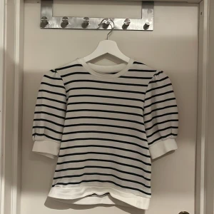 Randig topp från Holly & Whyte - Säljer en stilren vit och svart randig topp från Holly & Whyte by Lindex. Toppen har puffiga trekvartsärmar och en rund halsringning. Är i bra skick då jag bara har använt den ett par fåtal gånger.