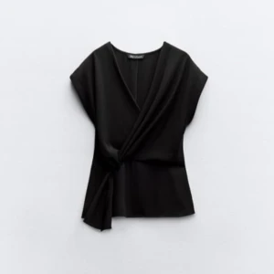 Svart omlottopp Zara - Elegant trendig svart omlottopp från Zara med v-ringning och knytning i sidan. Perfekt för en stilren look. Lapp kvar. Säljs inte längre, aldrig använd