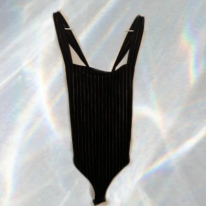 Svart randig body topp - Snygg svart body med guld ränder och korsade axelband i ryggen. Perfekt för en stilren look.