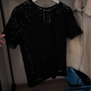 Svart spetsblus från Superdry - Snygg svart spetsblus från Superdry med korta ärmar. Perfekt för en elegant look med fina spetsdetaljer som ger en feminin touch. Passar bra till både jeans och kjol.