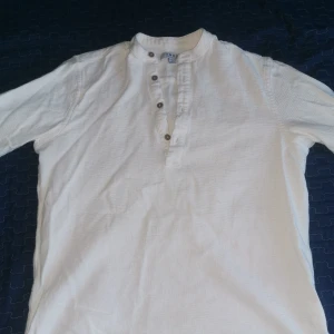 Vit skjorta från Smog - Säljer en vit skjorta från Smog i storlek M. Skjortan har en avslappnad passform med knappar framtill och en ståkrage. Perfekt för en stilren och bekväm look.
