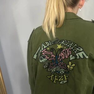 Grön jacka från Zadig & Voltaire - Snygg grön jacka från Zadig & Voltaire med coola broderade detaljer på ryggen. Jackan har långa ärmar och praktiska fickor framtill. Storlek s - m 