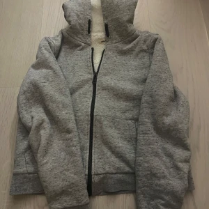 Grå hoodie med dragkedja och huva - Säljer en mysig grå hoodie med dragkedja och huva. Insidan är fodrad med mjuk fleece och baksidan har ett stort Z-mönster i glitter Perfekt för kyliga dagar eller om man bara vill vara varm 🩷 