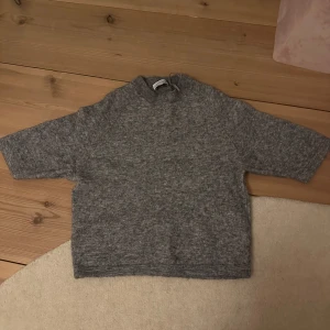 Grå stickad tröja - Mysig grå stickad tröja med trekvartsärm och hög krage. Perfekt för kyligare dagar och ger en avslappnad stil. Passar bra till jeans eller kjol.