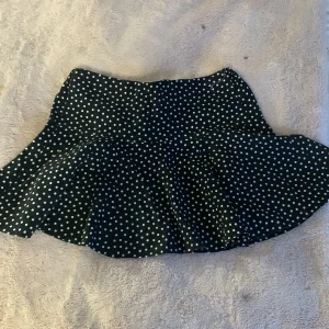 Svart kortkjol med vita prickar - Snygg svart kortkjol med vita prickar. Kjolen har en volangdetalj som ger den extra flärd. Perfekt för att lägga till en lekfull touch till din outfit. Denna kjol är ifrån Zara❤️