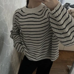 Randig stickad tröja - Säljer en mysig stickad tröja med svartvita ränder. Tröjan har en avslappnad passform och långa ärmar, perfekt för kyligare dagar. Den är både stilren och bekväm, ett måste i garderoben!