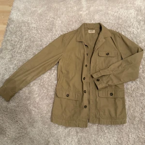 Beige jacka från East West - Snygg beige jacka från East West med knappar framtill och flera praktiska fickor. Perfekt för en stilren och avslappnad look. Jackan har långa ärmar och en klassisk krage.