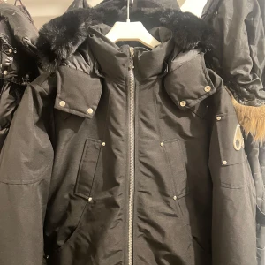 Moose Knuckles - Snygg svart Moose Knuckles med pälskantad huva och dragkedja framtill. Jackan har flera fickor och den är Perfekt för kalla vinterdagar. Jackan är helt ny. Kan byta mot en mocler cardigan sM. Priset kan diskuteras.