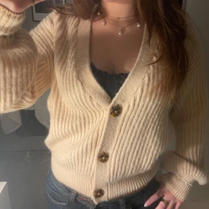 Beige ribbad kofta med knappar - Säljer en mysig beige kofta med ribbad struktur och stora knappar framtill. Perfekt för kyliga dagar och lätt att matcha med olika outfits. (Ull och alpacka)