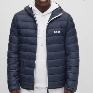 Mörkblå pufferjacka från BOSS.     Boss Green J_thor dark blue - Mörkblå pufferjacka från BOSS med dragkedja och huva. Ord pris 2699kr på boozt.com Jackan har ett stilrent, quiltat mönster och är perfekt för kyligare dagar. Den har långa ärmar och en boss logga på bröstet. Jackan är i nyskick och har inga besvärr köpt i mitten av november knappt använd. Vid föer information samt bilder kontakta via dm på varan!