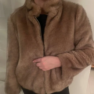 Beige/brun pälsjacka med dragkedja - Säljer en beige pälsjacka med dragkedja. Jackan har en hög krage och långa ärmar, väldigt varm. Väldigt stilren! 
