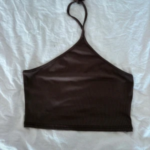 Brun ribbad halterneck topp - Snygg brun halterneck topp med ribbad struktur. Perfekt för en stilren look. Toppen är ärmlös och har en smickrande passform.