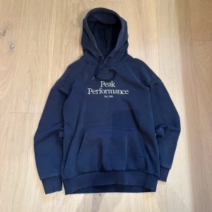 Mörkblå hoodie från Peak Performance - En stilren mörkblå hoodie av Peak Performance . Den har en  justerbar huva med snören. Perfekt för en avslappnad stil.