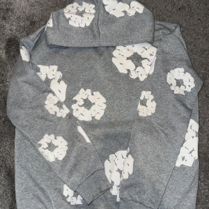 Grå hoodie med vita blommor - Säljer en grå hoodie med ett unikt blommönster i vitt. Tröjan har en bekväm passform och en klassisk huva. Perfekt för en avslappnad stil.