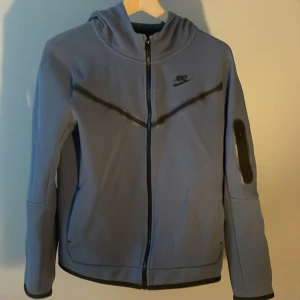 Nike tech blå - Nike tech som är från 158 till 170cm, skicket på tröjan är fint med inga skador eller något annat. Frågor eller funderingar är det bara att slå en pling!