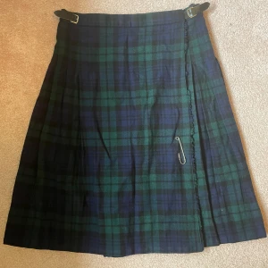 Kilt - Blå- och grönrutig kilt, made in England. Stängs med bälten och säkerhetsnål. Mått:  Midja 42-44 cm platt Längd 67 cm  