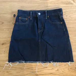 Mörkblå jeanskjol från Levi’s. Kjolen är ganska kort i modellen med normal midja. Storlek W25. Använd ett fåtal gånger och är därmed nästan som nyskick. 