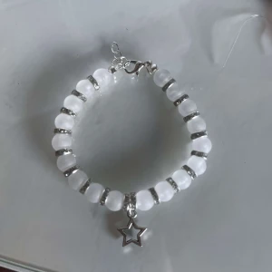 Vitt armband med stjärnhänge - Säljer ett superfint vitt armband med pärlor och ett gulligt stjärnhänge i silver. Armbandet har små silverdetaljer mellan pärlorna som ger det en extra touch. Perfekt för att piffa upp vilken outfit som helst! ✨