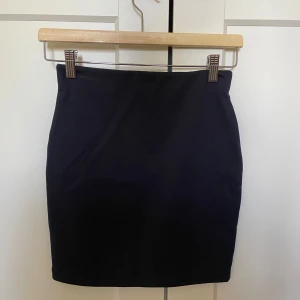 Svart kjol i storlek XS - Säljer en stilren mörkblå kjol i storlek XS. Perfekt för både vardag och fest! Kjolen har en enkel och elegant design som gör den lätt att matcha med olika toppar och accessoarer. Kjolen är knappt använd. 