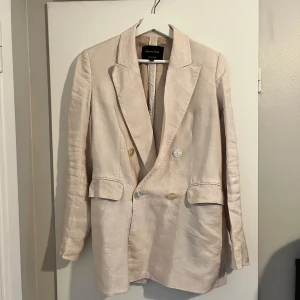 Beige kavaj från Massimo Dutti - Säljer en elegant beige kavaj från Massimo Dutti i storlek S. Kavajen är tillverkad i Portugal och har en klassisk design med dubbla knappar framtill. Den är långärmad och har en stilren passform som passar perfekt för både vardag och fest. Materialet känns lyxigt och ger en sofistikerad look.