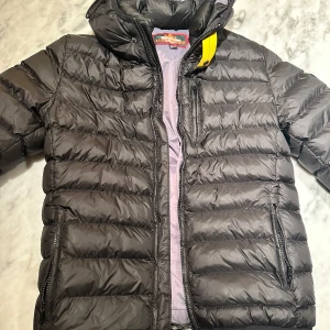 Svart pufferjacka från Parajumpers - Säljer en superlätt svart pufferjacka från Parajumpers i mycket bra skick. Jackan har en snygg quiltad design med dragkedja och en cool gul detalj vid kragen. Perfekt för höst och vinter, håller dig varm och stilren. Passar ungdomar i storlek 14-15 år. Pris kan absolut diskuteras 