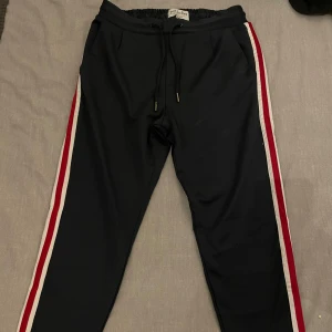 Eleganta trackpants från Just Junkies - Otroligt sköna samt snygga brallor från Just Junkies i storlek S, fint skick. En tidlös marinblå färg med vit/röda streck längs med hela sidorna som gör att byxorna verkligen poppar ut i verkligheten och funkar med allt till alla sammanhang! Ett plagg alla borde ha i garderoben🙌🏻