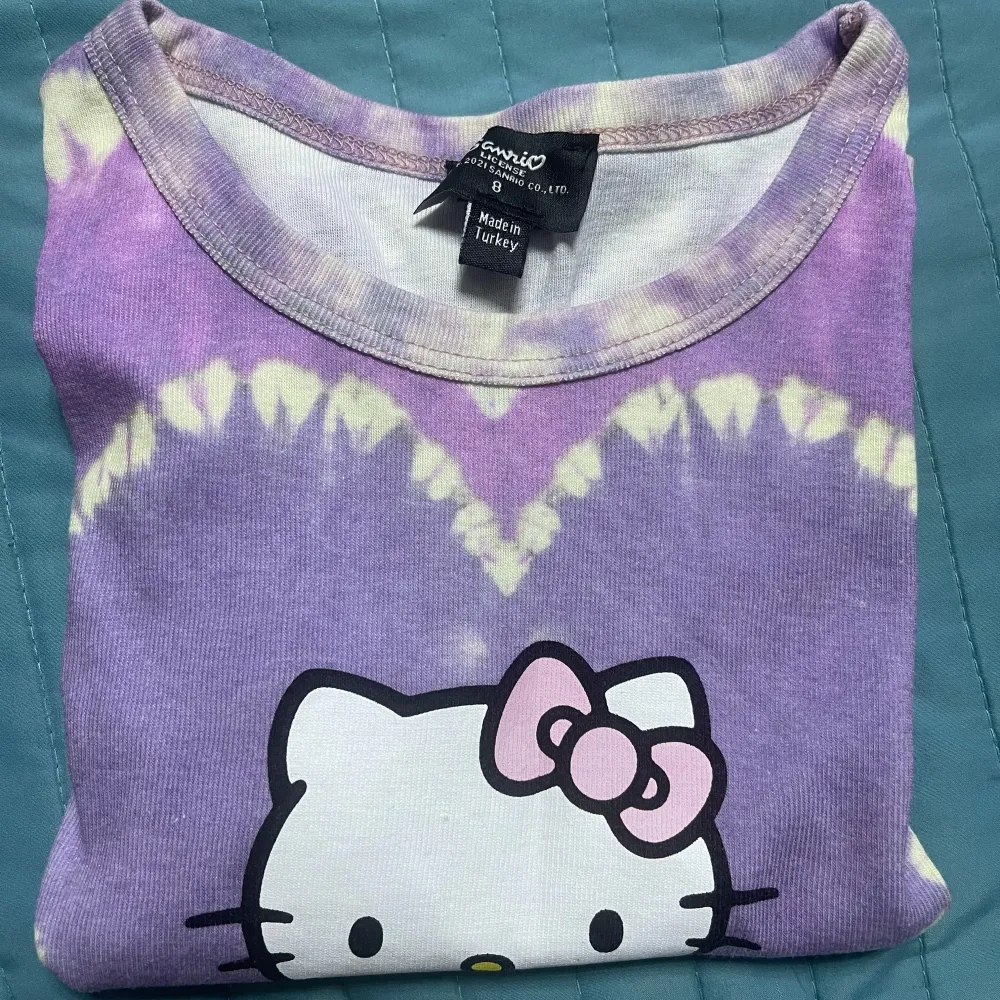 Supergullig lila croppad t-shirt med Hello Kitty-tryck och hjärtmönster.T-shirten har korta ärmar och är i mycket bra skick. Perfekt för alla Hello Kitty-fans! 💜. Toppar.