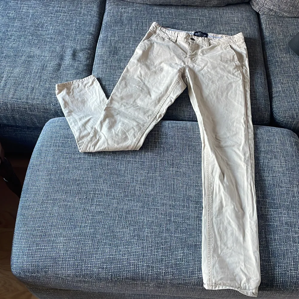 Säljer ett par stilrena beige byxor från Bondelid i storlek 30. De har en klassisk design med normal passform och är perfekta för både vardag och fest. Byxorna är i bra skick och har en snygg randig insida vid midjan. Perfekta för höst och vår! Pris går alltid att förhandlas!. Farkut & Housut.