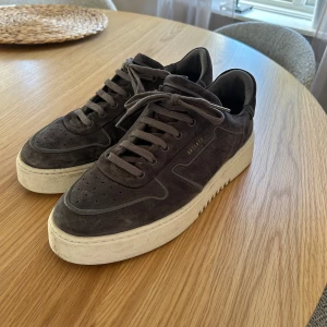 Grå sneakers från Axel Arigato - Säljer ett par snygga grå sneakers från Axel Arigato i mocka. De har en stilren design med snörning och en vit sula som ger en skön kontrast. Perfekta för både vardag och fest! 🕺