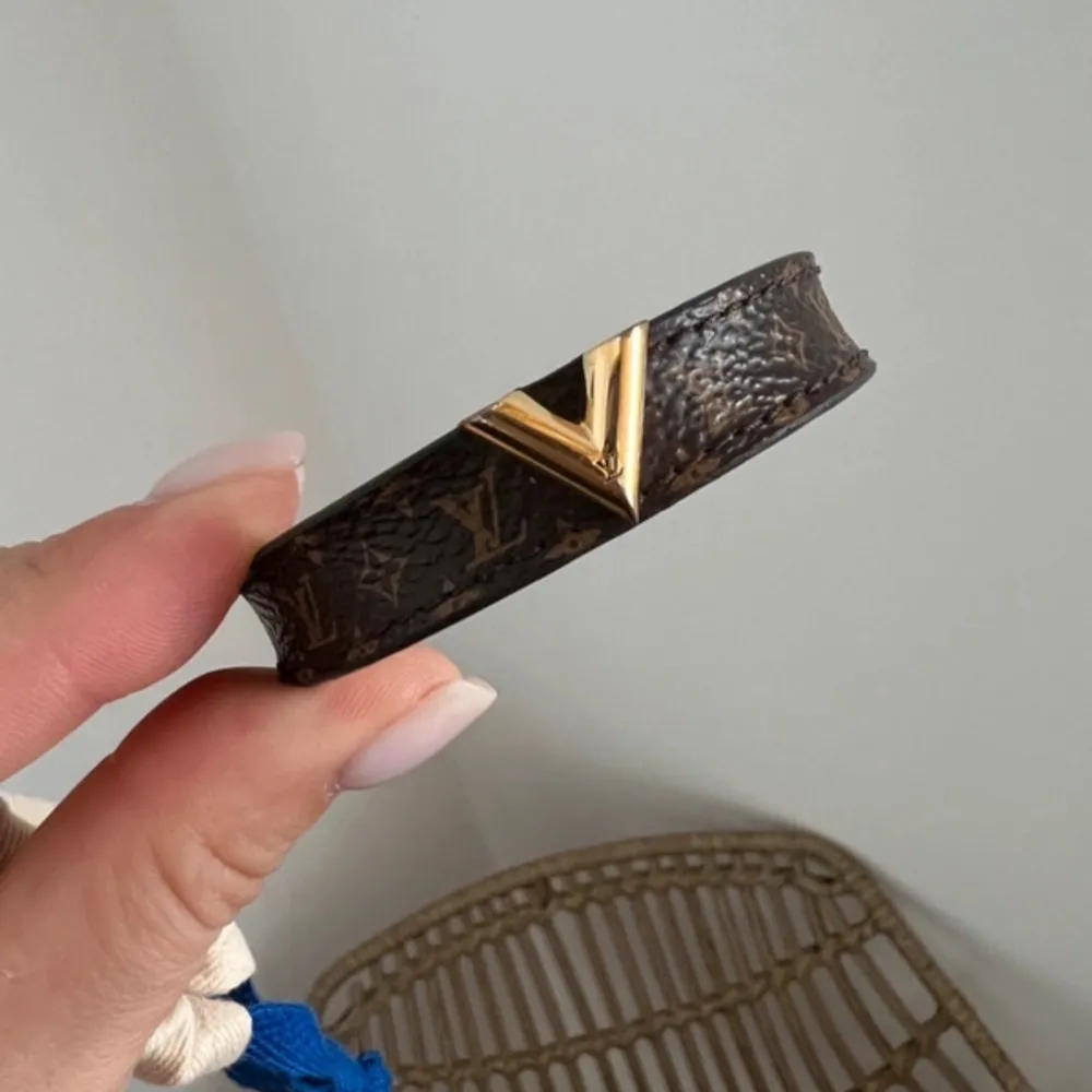 Säljer ett snyggt brunt armband från Louis Vuitton storlek 19, köpt i Vitkac. Armbandet har en elegant guldfärgad V-detalj och justerbar stängning, monogroniakt tryck.. Accessoarer.