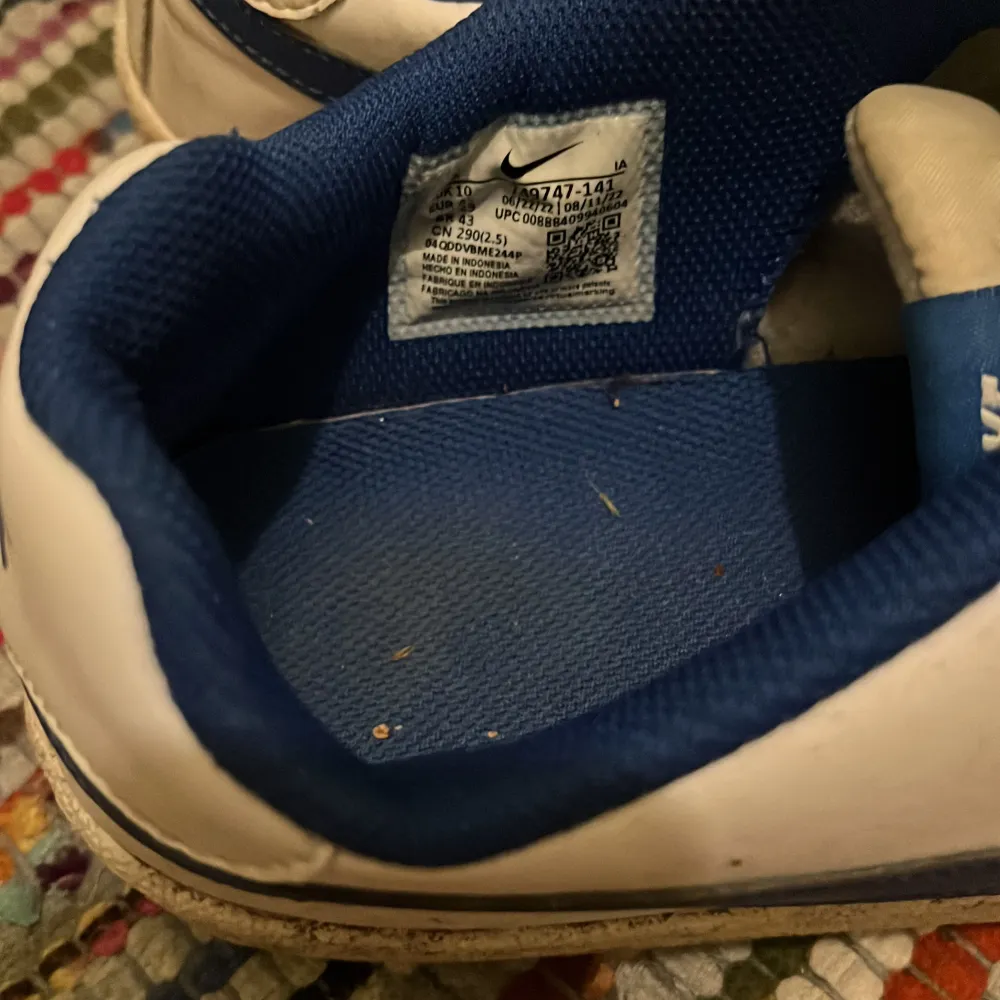 Säljer ett par vita Nike sneakers med blå detaljer. De har en klassisk design med snörning och är i bra skick, men lite smutsiga. Perfekta för vardagsbruk eller träning. Storleken är herr 45. . Skor.