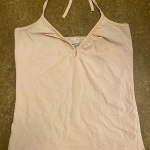 Ljusrosa halterneck-linne  - Säljer ett ljusrosa halterneck-linne från Gina Tricot i storlek XS. Perfekt för sommardagar med sin lätta och bekväma passform. Linnet har en enkel design med knytband i nacken och en liten v-ringning framtill.