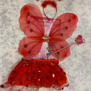 Röd fjärilsdräkt med vingar och kjol - Superfin röd fjärilsdräkt med glittriga vingar och en matchande kjol. Vingarna har stjärndetaljer och en glittrig blomma i mitten. Kjolen är täckt med paljetter för extra bling. Perfekt för maskerader eller lekfulla tillfällen! 🦋✨. Finns fler kvar, 125kr/paket                  Kan skicka med posten bara 