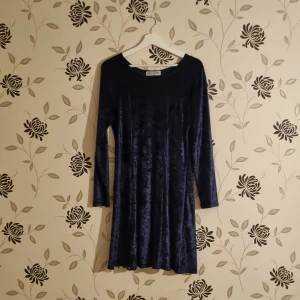 Mörkblå sammetklänning från Ewings Clothing - Snygg mörkblå klänning i sammet från Ewings Clothing. Den har en elegant, långärmad design och är perfekt för höst- och vinterfester. Klänningen har en mjuk och glansig yta som ger en lyxig känsla.