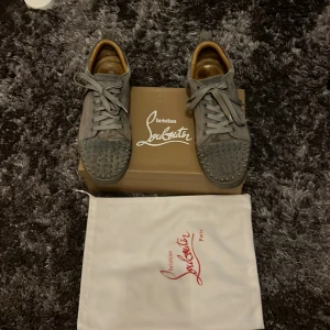 Grå sneakers från Christian Louboutin - Säljer ett par gråa skor från Christian Louboutin i bra skick. Köp dessa om du vill ha dem fetaste skorna bland dina vänner på festen🍾 Skorna har den ikoniska röda sulan och är dekorerade med nitar på ovansidan. Några og saker tillkommer. Osäker på äktheten men det är en äldre modell och han jag köpte dom av sa att de var äkta!🤘🍾