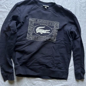 Mörkblå sweatshirt från Lacoste - Säljer en mörkblå sweatshirt från Lacoste med deras klassiska krokodillogo på bröstet. Tröjan har långa ärmar och är i mycket bra skick. Perfekt för en avslappnad stil eller för att hålla sig varm under kyligare dagar.