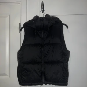Svart dunväst från Zara - Säljer en svart dunväst från Zara i mycket bra skick. Västen har en dragkedja framtill och en mysig huva, perfekt för kyliga dagar. Den är stilren och passar till de flesta outfits. Perfekt för höst och vinter!