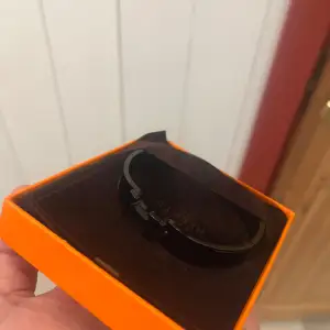 Säljer ett stilrent svart armband i metall. Det har en enkel och modern design med ett diskret lås. Perfekt för både vardag och fest! Kommer i en snygg orange ask. Äkta