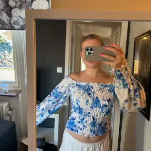 Supergullig vit offshoulder blus med blåa blommor, mittendelen samt ändarna på ärmarna i ribbat tyg🩵 Använd bara någon gång så i nytt skick🤍