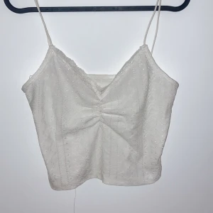 Vit spetslinne - Säljer ett sött vitt spetslinne med smala axelband. Linnet har en v-ringad design och är perfekt för sommardagar. Det är i mycket bra skick och passar både till vardags och festliga tillfällen.