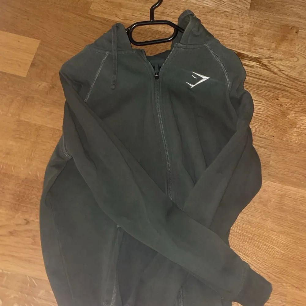 Säljer en grön hoodie från Gymshark i bra skick. Den har en dragkedja framtill och en justerbar huva. Perfekt för träning eller en avslappnad dag.  Tröjan är använd ett fåtal gånger. Hör av dig vid intresse!. Hoodies.