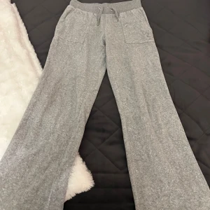 Grå mjukisbyxor från Juicy Couture - Superbekväma grå mjukisbyxor från Juicy Couture med breda ben. Byxorna har snörning i midjan, lågt pris pga att ena metall saken på snöret lossnat. Perfekta för en avslappnad dag hemma eller en chill dag ute. Fint skick annars men dom är något urtvättade. bra skick förutom snöret som jag beskrev. Stl 9-10 år.Nypris 850. 
