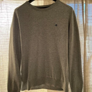 Grå, stickad tröja från Morris - Säljer en stilren grå tröja från Morris i 100% bomull. Den har en liten broderad logga på bröstet och ribbade muddar vid ärmslut och nederkant. Perfekt för både vardag och lite finare tillfällen. Skicka ett meddelande vid intresse!