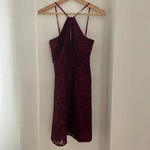Vinröd spetsklänning från New Look - Säljer en elegant vinröd klänning från New Look i storlek 6. Klänningen är i spets med ett vackert blommönster och har en smickrande passform. Den är axelbandslös med tunna band och en liten öppning fram. Perfekt för festliga tillfällen!
