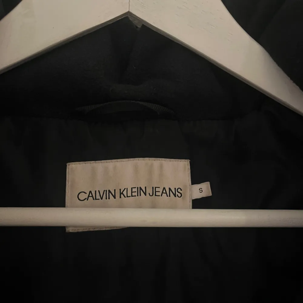 Säljer en snygg svart pufferjacka från Calvin Klein Jeans i storlek S. Jackan har en glansig finish och är perfekt för kalla dagar. Den har en dragkedja framtill och en mysig huva. Perfekt för vintern och hösten! Dragsko i kapuschongen åker ur ibland men har ingen påverkan på funktionen.. Jackor.